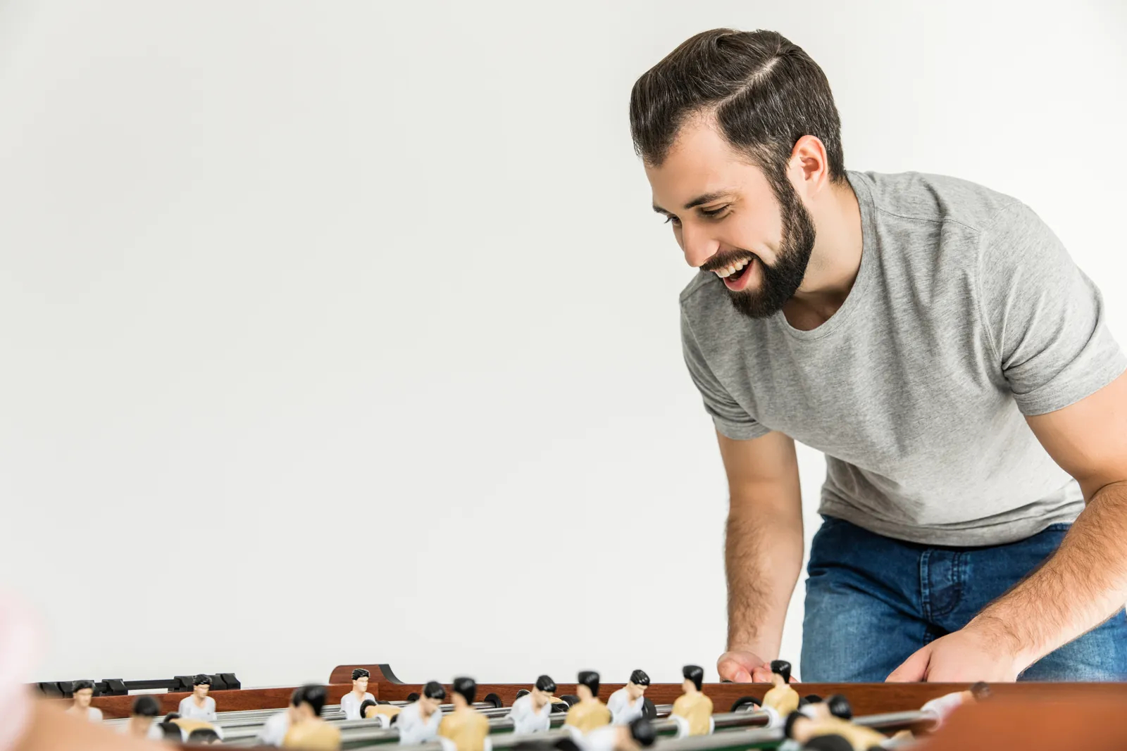 Ein Mann beugt sich lachend über einen Tischkicker und spielt.